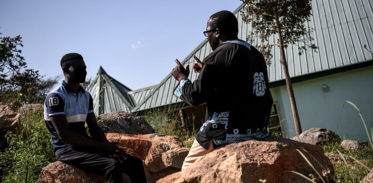 Zwei Männer aus Afrika sitzen auf großen Steinen und reden miteinander