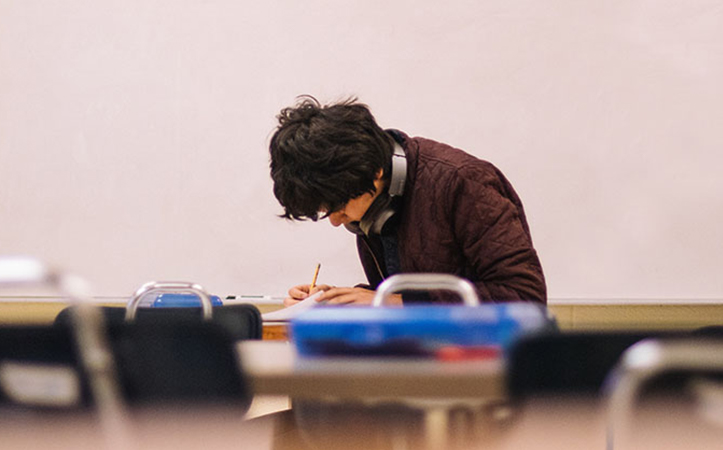 Ein Jugendlicher sitzt mit Kopfhörern an einem Tisch und schreibt