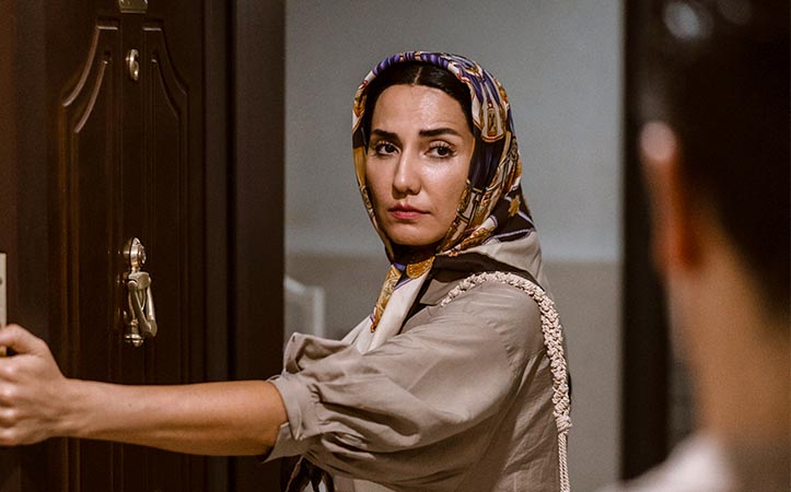 Muslimische Frau mit Kopftuch steht in einem Türrahmen gegenüber einem Mann und schließt die Tür.