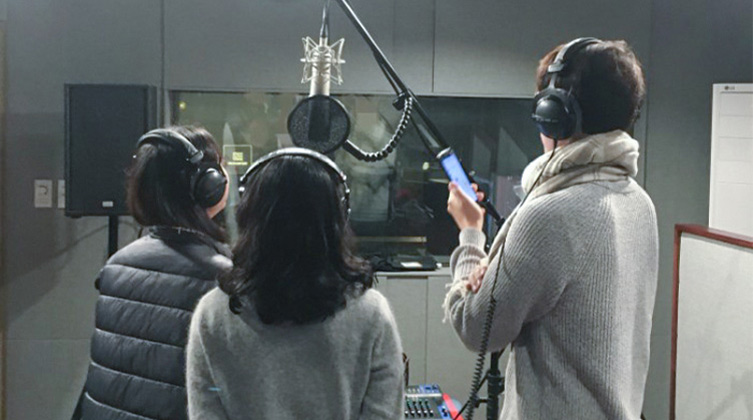 Drei Personen stehen in einem Soundstudio vor einem Mikrofon