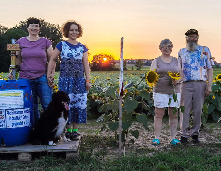 Ein älteres Ehepaar, deren Tochter, Enkelin und ein Hund vor einem Sonnenblumenfeld