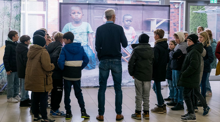 Eine Gruppe Kinder steht im Halbkreis mit einem Mann von hinten