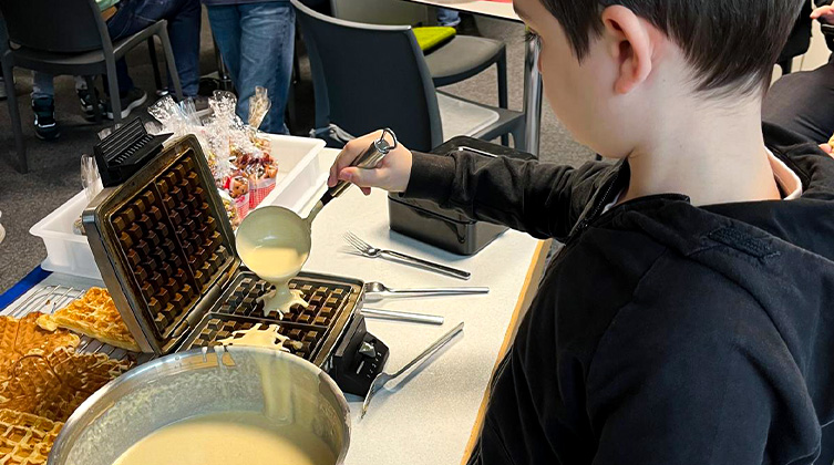 Seitenprofil eines Jungen der eine Kelle mit Teig auf ein Waffeleisen tut