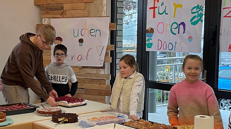 Einige Kinder stehen hinter Tischen auf denen Kuchen stehen