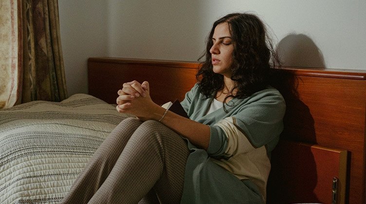 Eine Frau sitzt betend auf ihrem Bett.