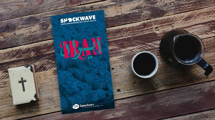 Abbildung der Shockwave-Box 2025 zu Iran auf einem Holztisch mit einer Bibel und einer Kafeetasse neben dem Materialpaket.