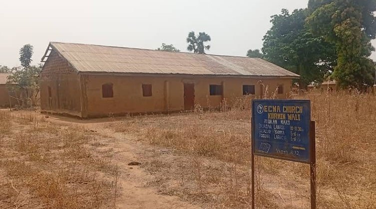 Ein Kirchengebäude aus Lehm steht auf einer trockenen Wiese