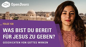 Brünette Frau mit leichtem Lächeln im altrosafarbenen Strickpullover vor einer Stadt mit weißen Gebäuden