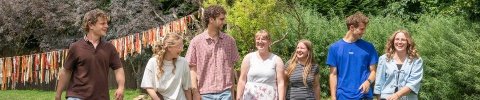 Eine Gruppe von sieben jungen Menschen in einem Garten mit einer Wimpelkette