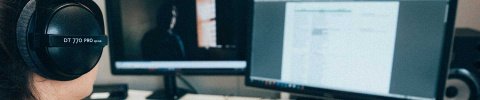 Frau mit Kopfhörern vor zwei Computerbildschirmen