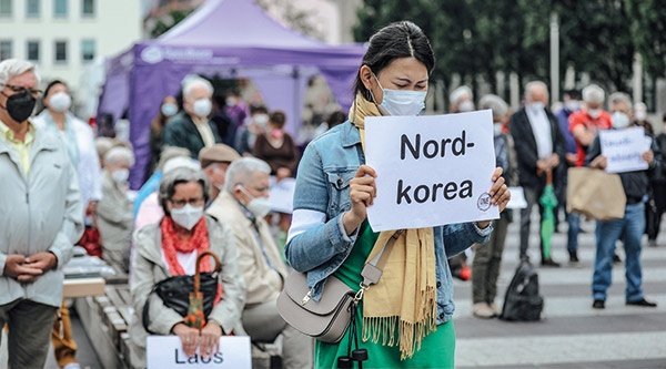 Frau hält ein Schild mit der Aufschrift "Nordkorea" in der Hand und betet