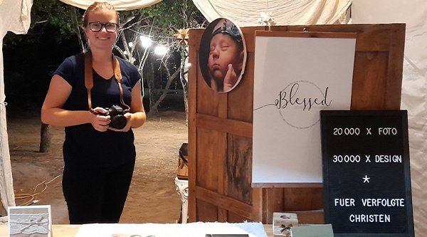 Eine Frau mit einer Kamera in der Hand steht vor einem Fotostand