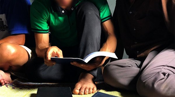 Drei Personen sitzen auf dem Boden und schauen in ein Buch 
