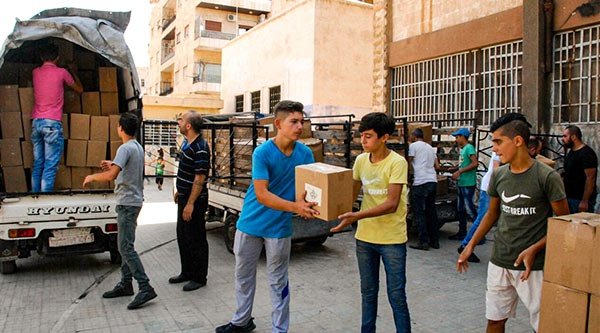 Syrische Jugendliche helfen beim Entladen von Lebensmittelpaketen aus einem Lastwagen