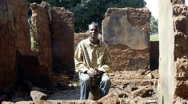 Afrikanischer Mann sitzt vor einem zerstörten Haus
