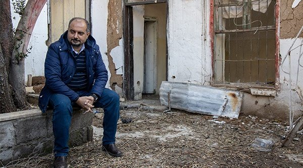 Ein syrischer Pastor sitzt auf einer kleinen Mauer vor seinem zerstörten Haus und Laden