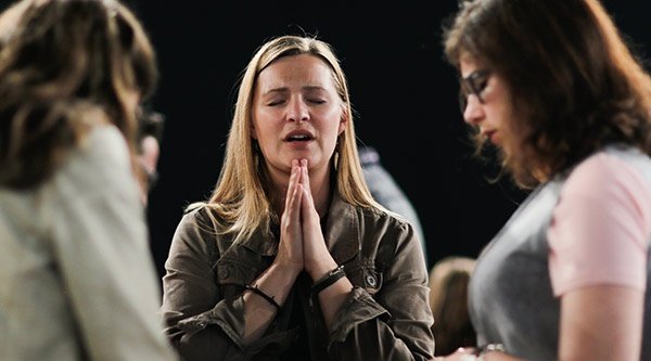 Junge Frau betet im Kreis mit anderen Christen