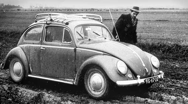 Ein Mann steht neben einem Käfer als schwarzweiß Bild