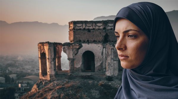 Das Gesicht einer blau-verschleierten Frau vor einer zerstörten Kirche auf einem Berg, die in Morgengrauen gehüllt ist