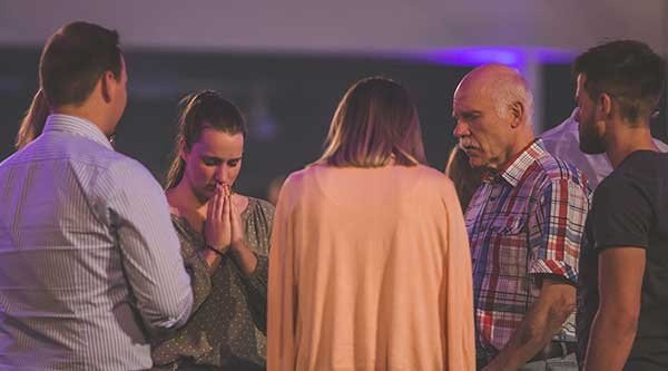 Eine Gruppe von Menschen gemischten Alters steht zusammen im Gebet für verfolgte Christen
