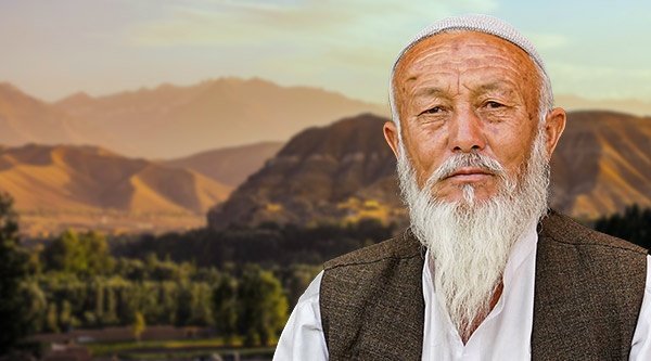 Afghanischer Mann mit weißem Bart und einem ernsten Gesichtsausdruck. Im Hintergrund Berge.