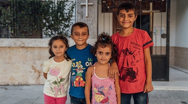 Vier Kinder stehen in bunten Klamotten vor einem Kirchengebäude