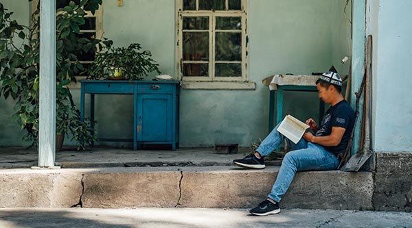 Ein Junge sitzt vor einem Haus und liest in einem Buch