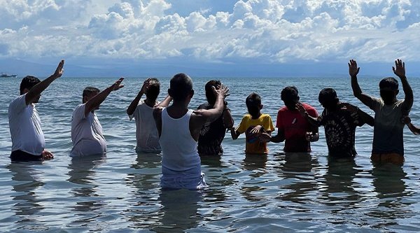 Mehrere Täuflinge stehen im Wasser und vor ihnen steht ein Mann im weißen Oberteil