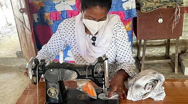 Indische Frau mit Mund und Nasenmaske arbeitet an einer Nähmaschine