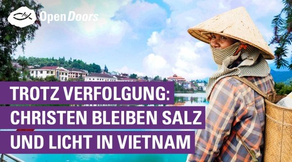 Eine Person mit einem vietnamesischen Hut auf dem Kopf steht vor blauem Gewässer und im Hintergrund sind einige große Häuser zu sehen