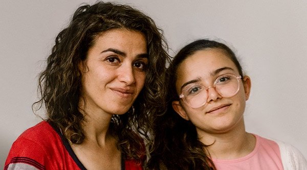 Eine Frau mit dunklen Haaren und ein Mädchen mit einer Brille schauen in die Kamera