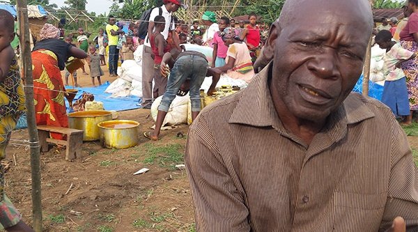 Im Vordergrung ein Kongolese mit kritischem Blick un dim Hintergrund viele Menschen, die gemeinsam essen 