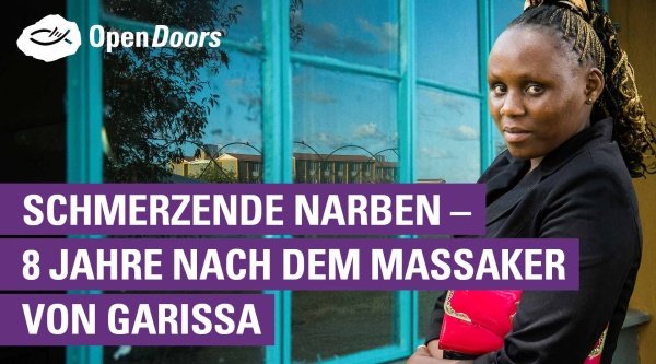 Eine Frau im schwarzen Oberteil mit einer roten Tasche im Arm steht an einem Fenster mit türkisfarbenem Rahmen