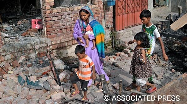 Eine Christin läuft mit ihren Kindern in Jaranwala durch die Trümmer eines von einer aufgebrachten Menschenmenge zerstörten Hauses