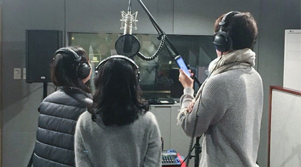 Drei Personen stehen in einem Soundstudio vor einem Mikrofon