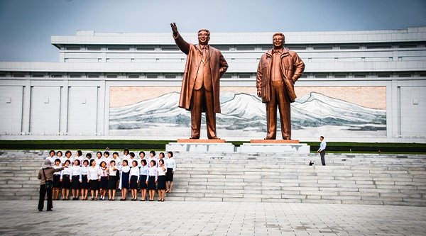 Eine Gruppe Menschen steht vor steinernen Treppen und hinter ihnen sind zwei Statuen zu sehen