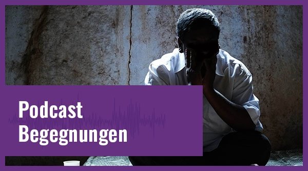Ein indischer Mann sitzt im Dunkeln in einem Raum mit unbearbeiteter Steinwand