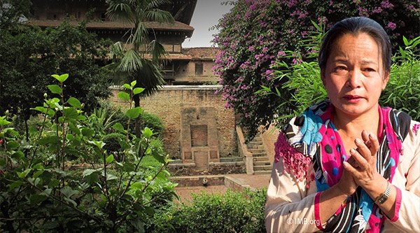 Eine asiatische Frau klatscht in die Hände und hinter ihr ist ein großer Blütenbaum und ein Steinhaus