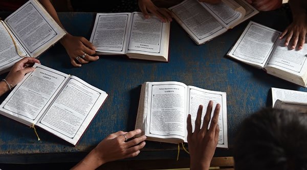 Verschiedene Bibeln liegen auf einem Tisch und Hände von Personen sind an den Bibeln zu sehen