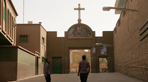 Zwei junge Männer stehen vor einem großen Tor darüber ein großes  Kreuz