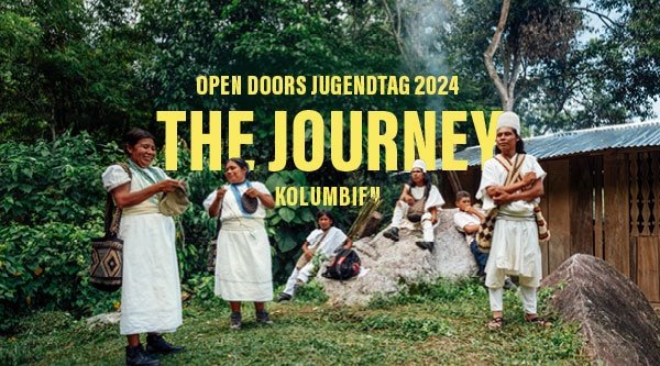 Eine Gruppe der indigenen kolumbischen Bevölkerung in weißer Tracht steht vor einem Wald und einer Hütte, dazwischen die Überschrift der Open Doors Tage 2024 zu Kolumbien