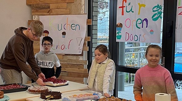 Kinder stehen hinter Tischen mit Kuchen darauf