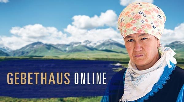 Eine ältere Frau mit Kopfbedeckung steht vor einer weiten Landschaft