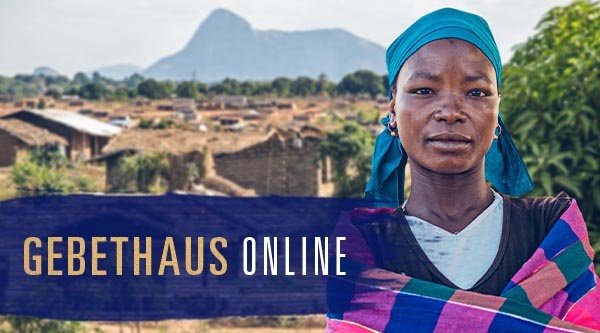 Eine afrikanische Frau mit Kopftuch im Hintergrund ein Dorf