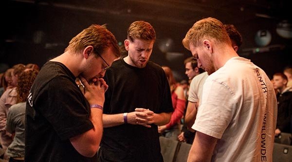 Drei junge Männer beten in einer Kleinergruppe bei einer Veranstaltung