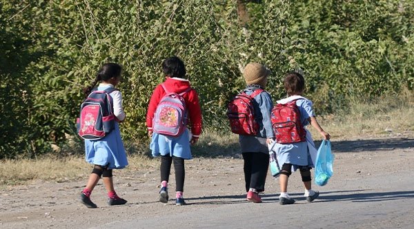 Vier junge Kinder laufen mit ihren Schultaschen auf dem Rücken eine Straße entlang