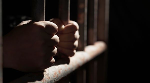 Zwei Hände greifen an die Gitterstangen eines Gefängnisses.