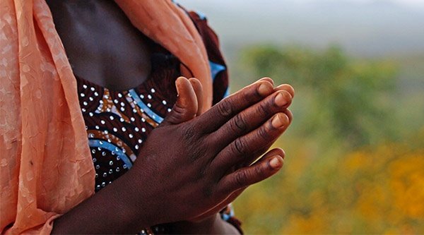 Eine afrikanische Frau faltet ihre Hände zum Gebet vor einer grünen Landschaft