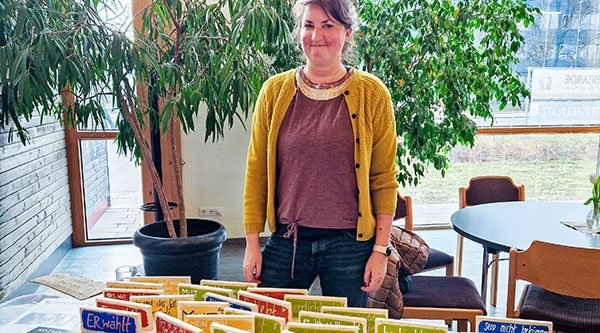 Frau steht hinter einem Tisch vor einer Raumpflanze 