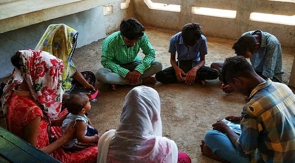 Indische Menschen sitzen im Kreis auf dem Boden und haben ihre Köpfe geneigt